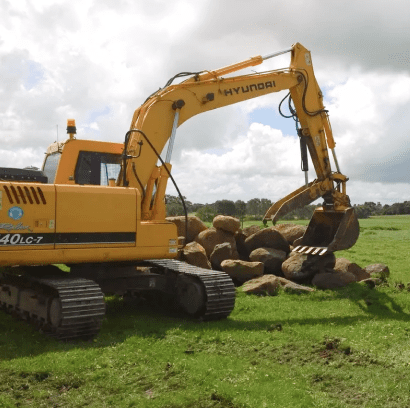 Yellow excavator moving rocks on grass field.
