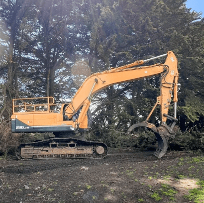 Excavator with claw attachment near trees.